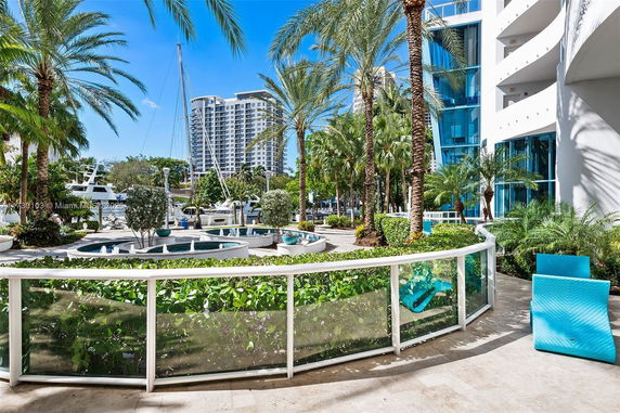View of outdoor area with palm trees, a building, and yachts docked nearby.