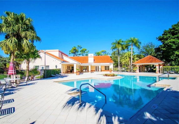 Outdoor swimming pool area with adjacent building and tiled roofs.
