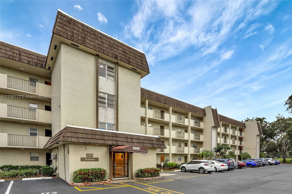 Front view of a multi-story residential building with balconies and parking spaces.