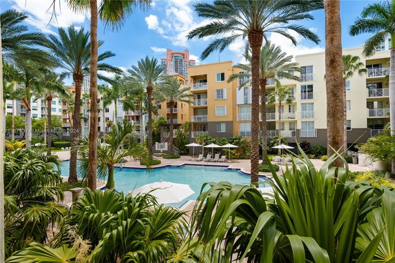 Outdoor view of a residential complex featuring palm trees and a swimming pool.