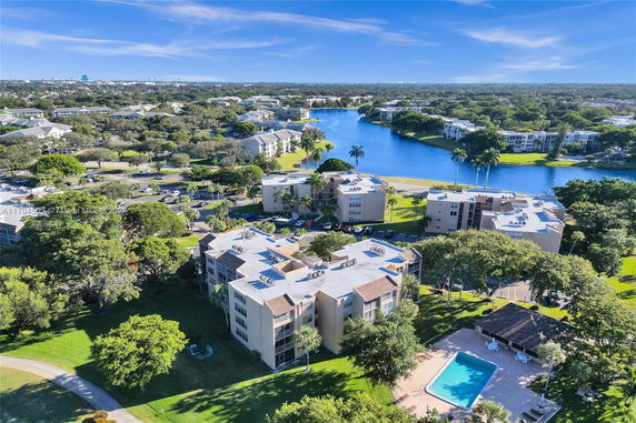 Aerial view of residential buildings surrounded by lush greenery and a lake.
