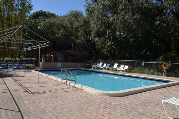 Outdoor swimming pool with surrounding lounge chairs and trees.