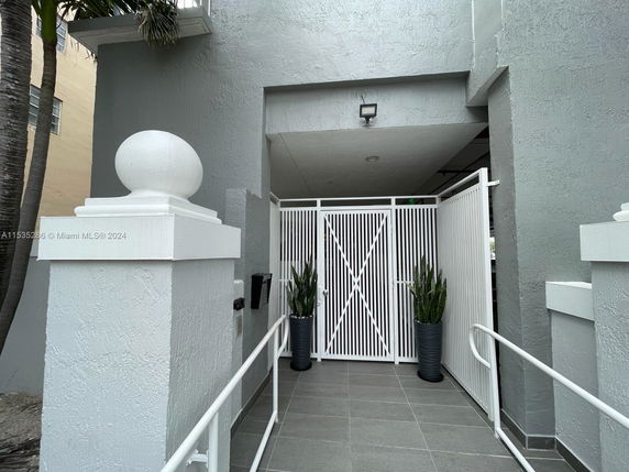 Entrance view of a building with a white gated entry and potted plants.