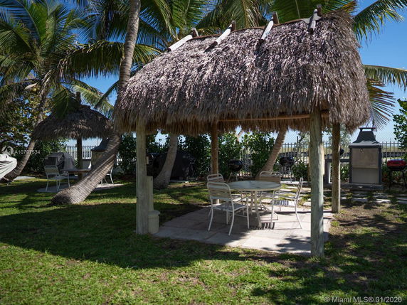 Outdoor area with a thatched-roof gazebo and seating surrounded by palm trees.