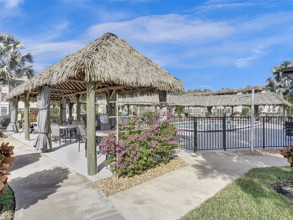 Outdoor swimming pool area with a thatched roof pavilion and seating.