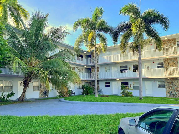 Front view of a three-story building with outdoor corridors and palm trees.