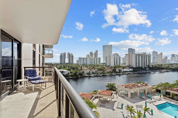 Balcony view from a high-rise building overlooking a river, distant cityscape, and swimming pool below.