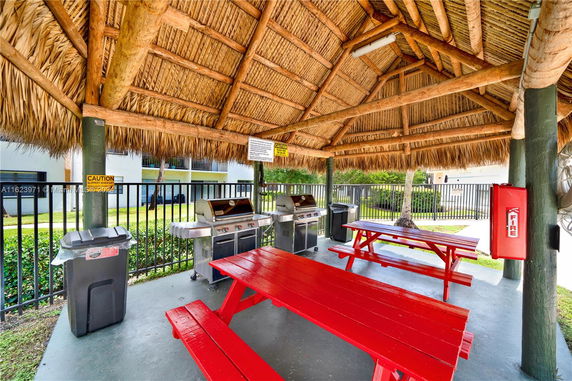 Outdoor area with picnic tables and barbecue grills under a thatched roof.
