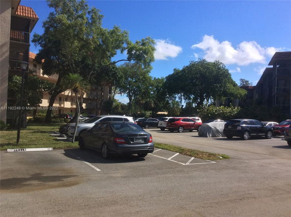 Outdoor parking area with several parked cars and adjacent residential buildings.