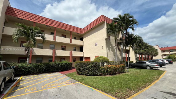 Front view of a multi-story building with red roof tiles and parking area.