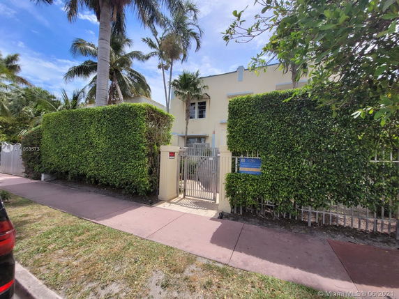 Front view of a house with a gated entrance and tall hedges.