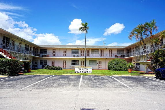 Front view of a two-story building with multiple units and a parking area in front.