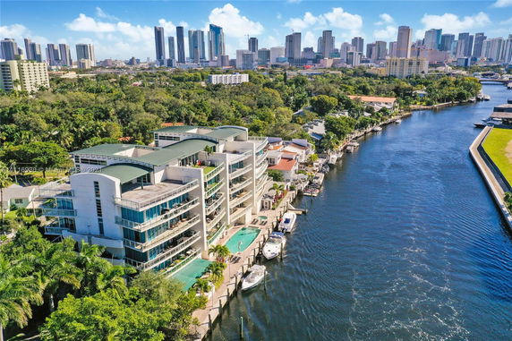 Aerial view of waterfront buildings with city skyline in the background.