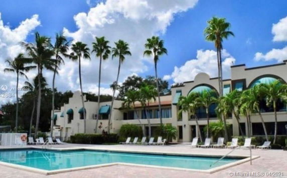 View of a swimming pool in front of a multi-story building with palm trees.