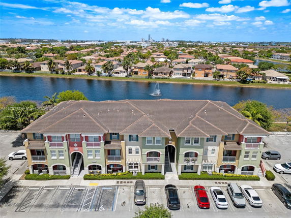 Front view of a multi-story residential building with multiple entrances and balconies, adjacent to a parking area.