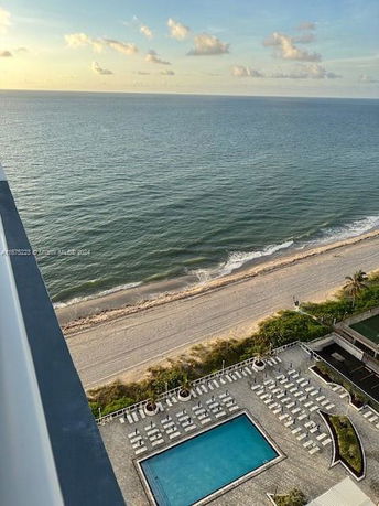 Panoramic view of a coastal area from a high vantage point, featuring a beachside swimming pool, sunbathing area, and the ocean.