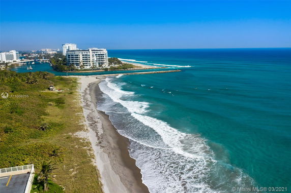 Aerial view of coastline with a beach and ocean, adjacent to a white multi-story building complex.