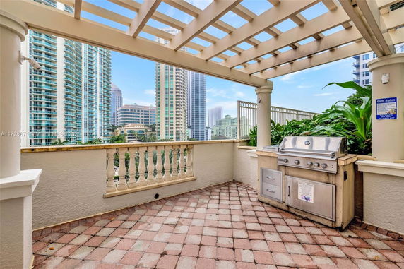 Rooftop area with a barbecue grill and pergola, overlooking a cityscape with tall buildings.
