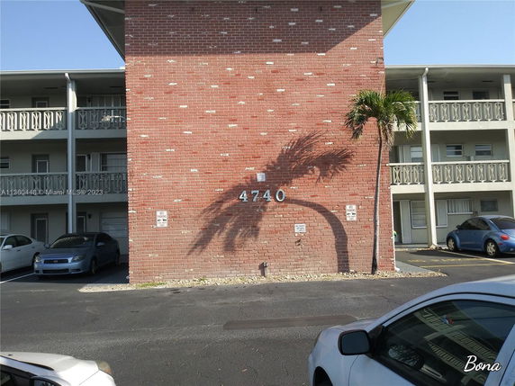 Front view of a brick building with balconies and a parking area.