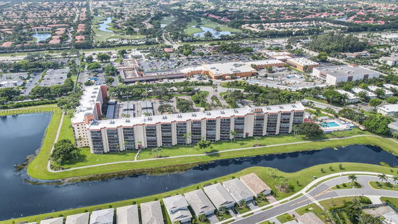 Aerial view of a multi-story residential building near a canal, surrounded by a large neighborhood and commercial area.
