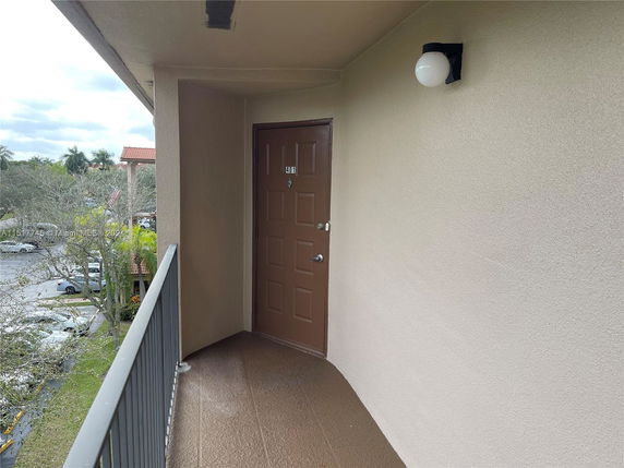 Exterior corridor with a view over a parking area and trees.