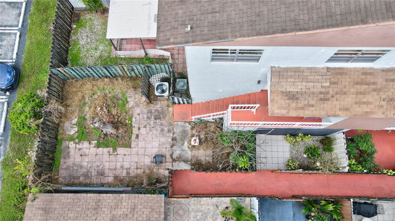 Top view of a building with a brown shingle roof, adjacent patio space, and small garden areas.