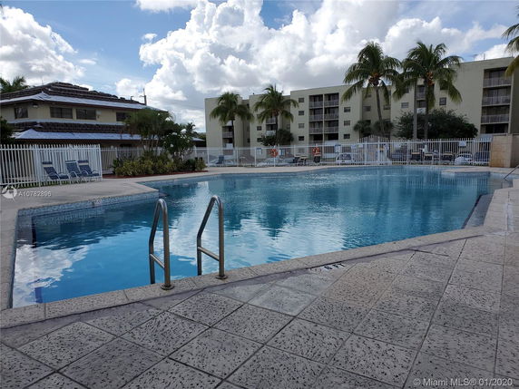 View of a recreational area with a swimming pool surrounded by buildings and palm trees.