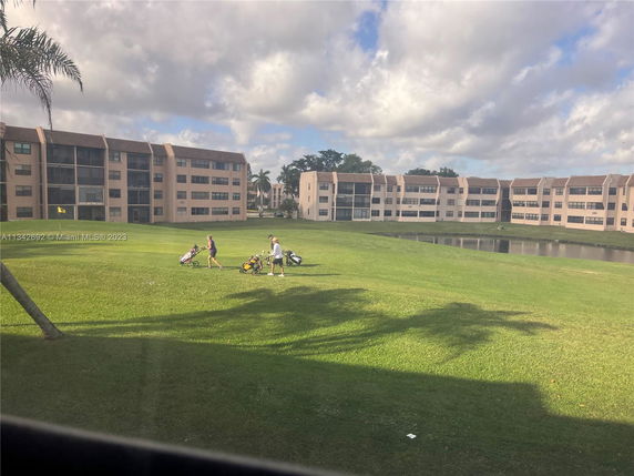 View of multiple residential buildings surrounding a grassy area with a small pond.