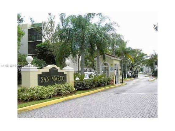 Front view of a building complex entrance with palm trees and signage.