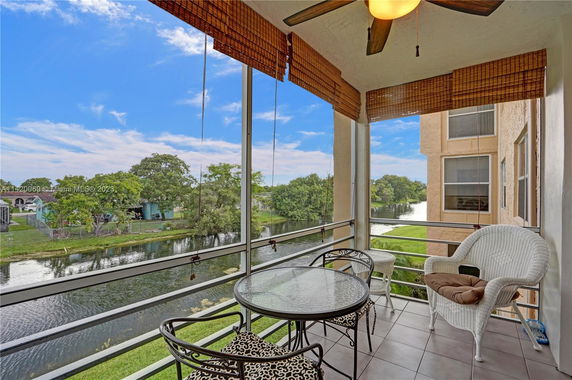 View from an enclosed balcony featuring outdoor furniture overlooking a canal and surrounding greenery.