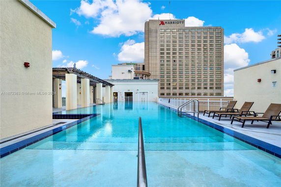 Rooftop swimming pool with lounge chairs and a view of a nearby building.