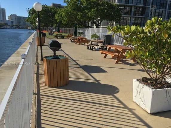 Outdoor area with picnic tables and a waterfront view, surrounded by buildings and trees.