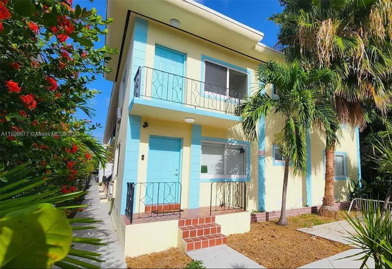 Front view of a two-story house with a light blue and yellow color scheme and a small balcony.