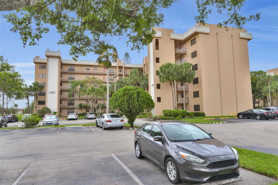 Front view of a multi-story residential building with balconies and a parking area in front.