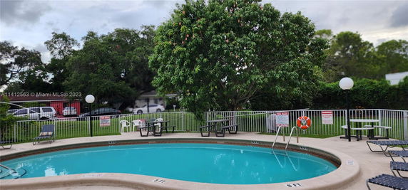 Outdoor swimming pool area with surrounding fence, trees, and seating.