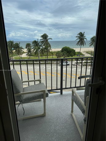 View from a balcony overlooking a beach with palm trees and ocean waves.