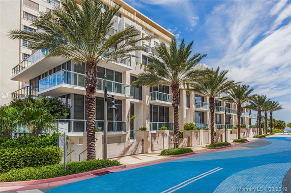 Front view of a multi-story building with balconies and palm trees.