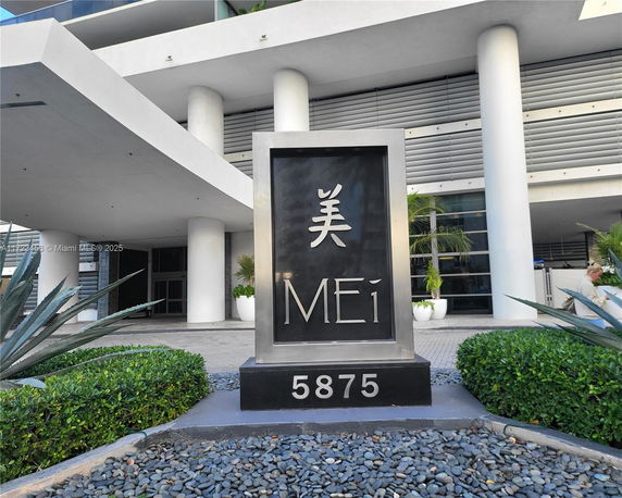 Front entrance of a modern building with large white pillars and a sign displaying 'MEi 5875'.