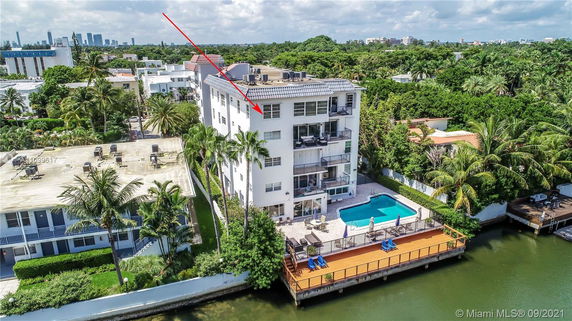 Aerial view of a multi-story residential building with balconies and a swimming pool, surrounded by lush greenery.