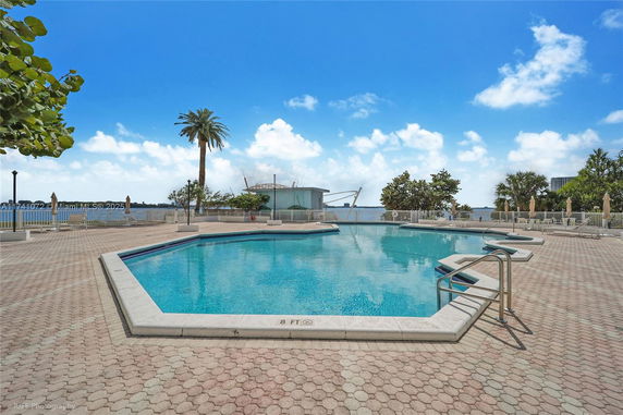 Outdoor swimming pool area with surrounding trees and a view of the water.