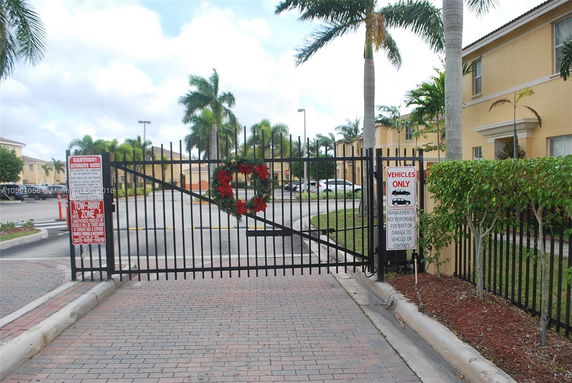 View of a gated parking area with surrounding buildings and palm trees.