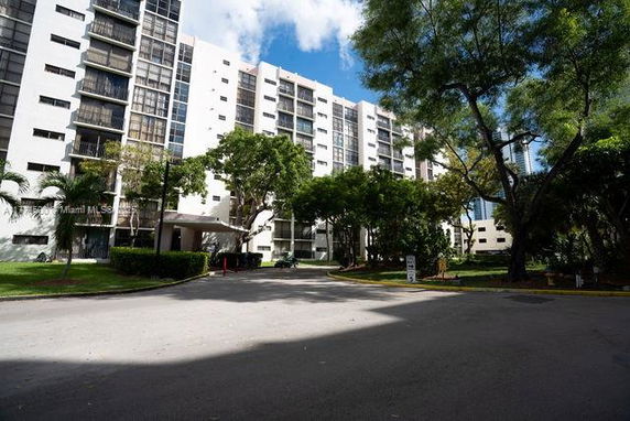 Front view of a multi-story residential building with balconies and surrounding trees.
