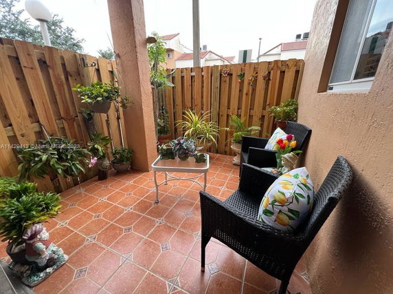 Small outdoor patio with terracotta tiles, wicker chairs, and potted plants.