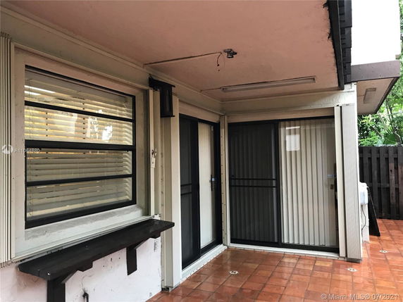 View of a house exterior with sliding glass doors and windows with blinds, tiled patio area.