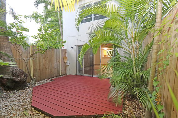 Back view of a two-story house with wooden deck and sliding glass door, surrounded by a wooden fence and greenery.