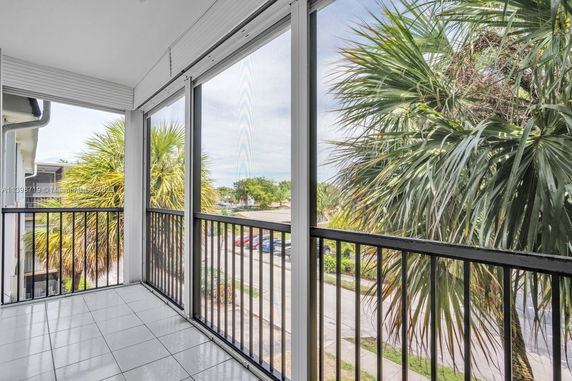 View from a screened balcony showing nearby street and palm trees.