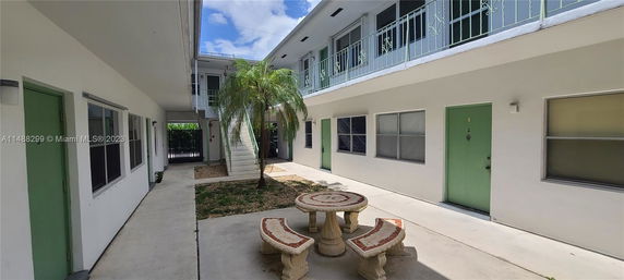 Courtyard view of a two-story apartment building with green doors and railings.