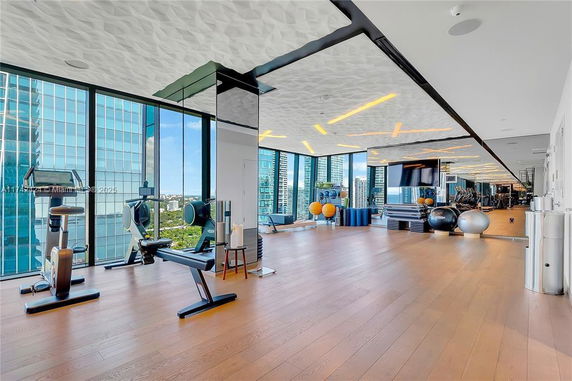Interior view of a modern gym area with fitness equipment and large windows.