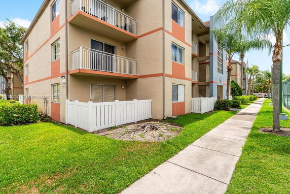 Front view of a three-story apartment building with balconies and a fenced area.