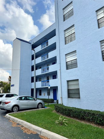 Front view of a multi-story apartment building with balconies and parked cars.
